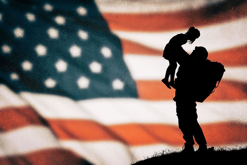 Silhouette of a solider holding a child in front of the US Flag